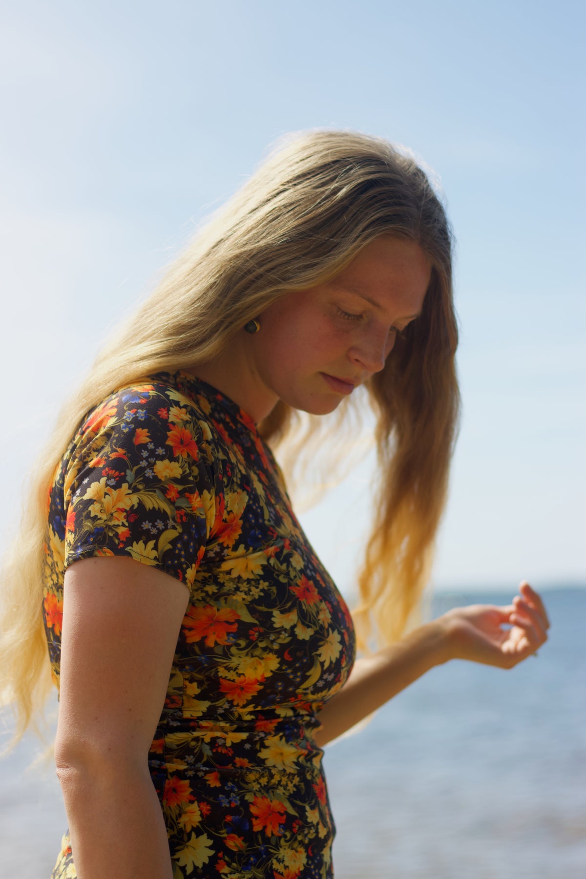 Woman in a colorful swimdress standing by the ocean with a clear blue sky.