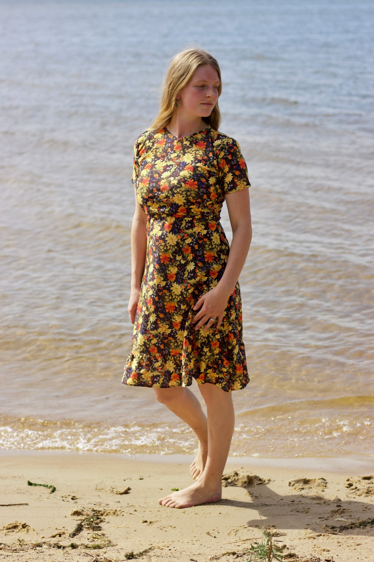 Woman in a floral dress standing on a beach with water in the background