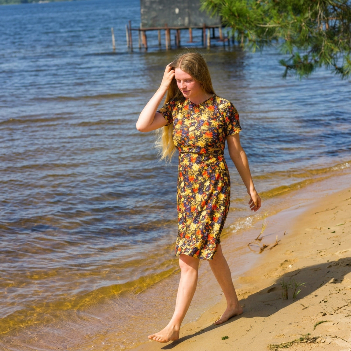 Woman in a floral modest swim dress walking along a beach with water and trees in the background