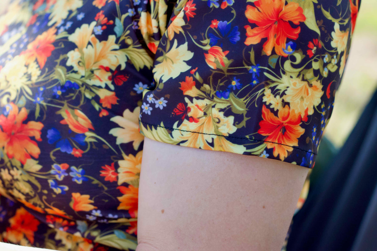 Close-up of a lady wearing a short-sleeve  modest swim top with a dark navy floral print featuring orange, yellow, and blue flowers.