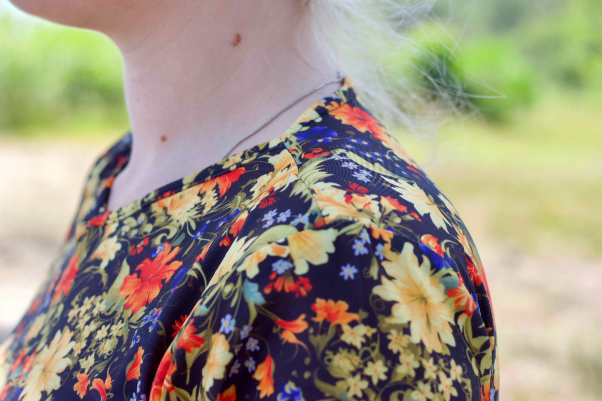 Close-up of a person wearing a dark navy floral swim top with yellow, orange, and blue flowers, photographed outdoors with a blurred green background.